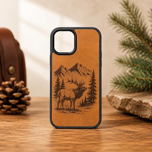 May include: A black smartphone case featuring a tan-colored back panel with a detailed black laser-engraved illustration of an elk standing in a forest with mountains in the background. The case has a square camera cutout at the top left corner.