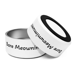 May include: Two white pet food bowls with the text "Bare Meownimum!" in black. One bowl is partially covering the other. The interior of the bowls is silver, and the top rim of the top bowl is black.