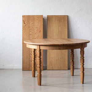 Peut inclure: Une table ronde en bois avec quatre pieds tournés et une finition brun clair. Deux panneaux de bois se trouvent derrière la table. La table mesure environ 76 cm de diamètre.