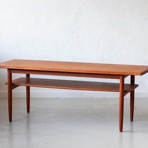Peut inclure: Une table basse de style moderne du milieu du siècle, en bois, avec une étagère inférieure. La table a un plateau rectangulaire et une finition brun clair.