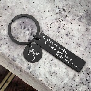 May include: Black metal keychain with a small round charm that says "love you" and a rectangular charm that says "Drive safe. I need you here with me".
