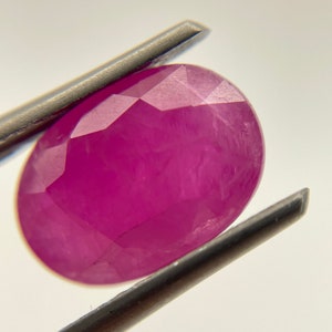 Op de afbeelding: Een levendige roze ovaalvormige edelsteen met een facetgeslepen vorm. De edelsteen wordt vastgehouden door een pincet.