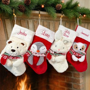Op de afbeelding: Vier kerstsokken met pluche dierenfiguren, waaronder een ijsbeer, pingu&iuml;n, konijn en vos. Elke sok heeft een witte boord die is geborduurd met de namen Jaden, Luna, Lily Rose en Immanuel in een rood lettertype.