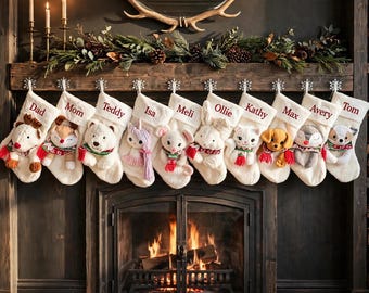 Op de afbeelding: Tien crèmekleurige kerstsokken hangen op een rij, elk voorzien van een pluche dierfiguur en een in rood geborduurde naam: Dad, Mom, Teddy, Isa, Meli, Ollie, Kathy, Max, Avery en Tom. De sokken hangen aan zilverkleurige sneeuwvlokhaken.