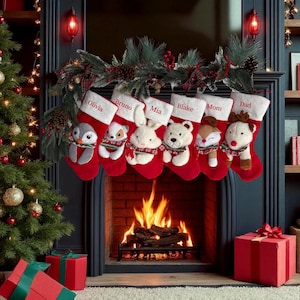 Op de afbeelding: Zes rode kerstsokken met witte boorden, elk voorzien van een pluche dier en een in rood geborduurde naam: Olivia, Bruno, Mia, Blake, Mom en Dad. De sokken hangen aan een groene slinger boven een open haard.