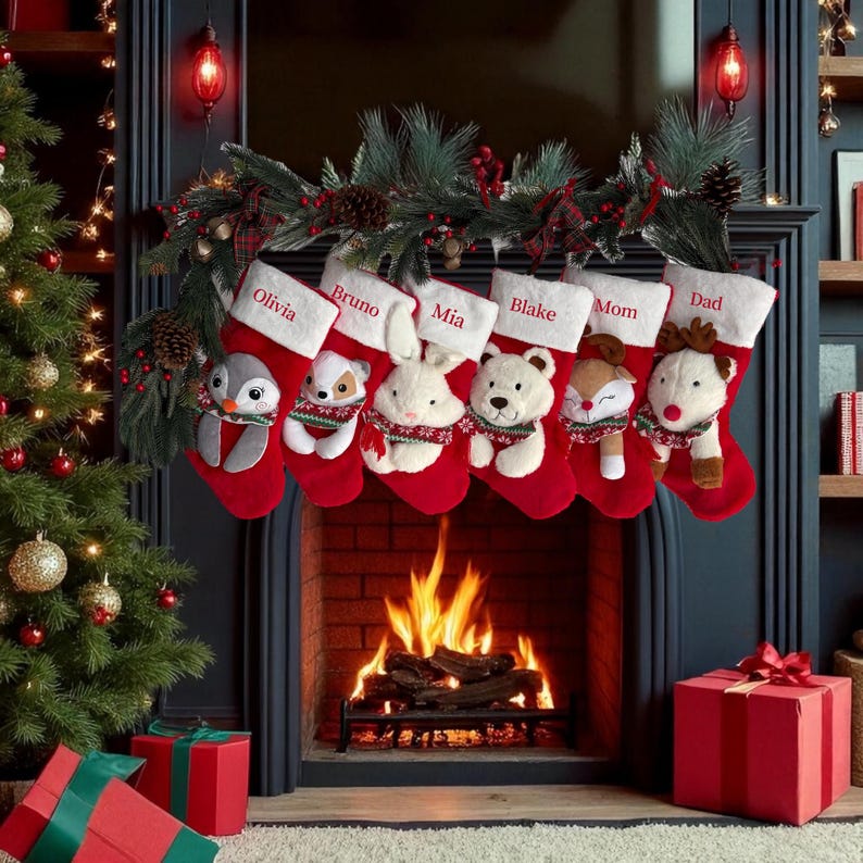 Op de afbeelding: Zes rode kerstsokken met witte boorden, elk voorzien van een pluche dier en een in rood geborduurde naam: Olivia, Bruno, Mia, Blake, Mom en Dad. De sokken hangen aan een groene slinger boven een open haard.