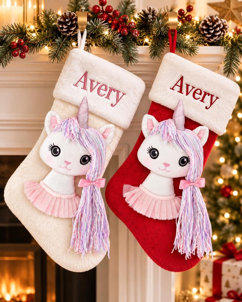 Op de afbeelding: Twee pluche kerstsokken, &eacute;&eacute;n cr&egrave;me en &eacute;&eacute;n rood, elk met een witte rand van imitatiebont geborduurd met de naam Avery in het rood. Een witte eenhoornapplicatie met een roze tutu, een zilveren hoorn en lang haar van pastelkleurig garen.
