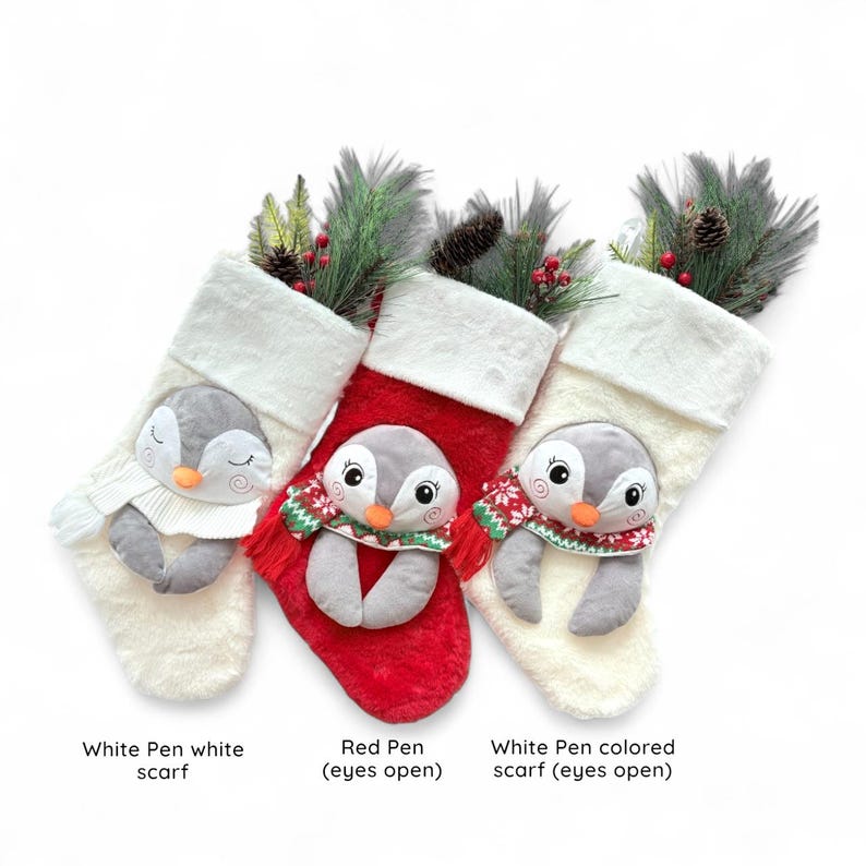 Op de afbeelding: Drie kerstsokken met pluche pingu&iuml;napplicaties. E&eacute;n is wit met een witte sjaal, &eacute;&eacute;n is rood met een sjaal met patroon, en &eacute;&eacute;n is wit met een sjaal met patroon. Elke sok heeft een witte rand van imitatiebont en dennentakken.