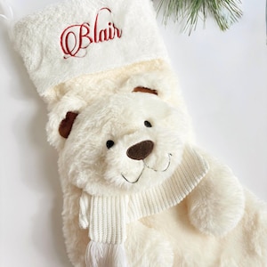 May include: A plush, cream-colored Christmas stocking with a polar bear design. The bear has a brown nose and ears, and wears a white scarf. The name "Blair" is embroidered in red on the cuff.