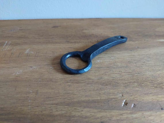 A bottle opener actually hammered into shape by a blacksmith — you can see the forge marks, and no two are exactly alike; it's functional sculpture.