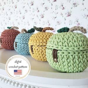 May include: Four crocheted apple-shaped containers in shades of red, blue, yellow, and green. Each has a brown stem and a leather strap. The image includes text that says "digital crochet pattern" and "English".