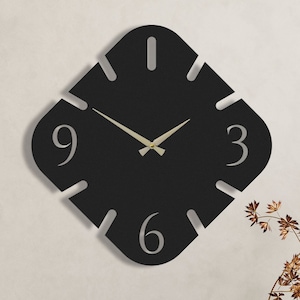 May include: Black square clock with silver hands and white numbers on a white wall. The clock is hanging above a wooden cabinet.