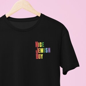Peut inclure: T-shirt noir avec le texte "NICE JEWISH BOY" en couleurs arc-en-ciel.