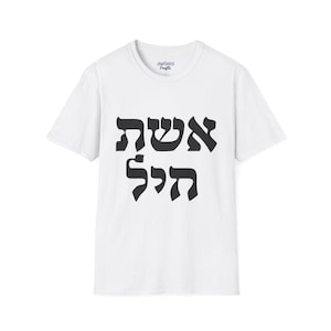 May include: A white short-sleeved t-shirt featuring black Hebrew text printed on the center of the chest. The text reads "אשת חיל". The shirt has a crew neckline and a brand label printed on the inside of the collar area that reads "Jewniverse Crafts".