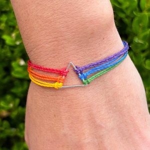May include: A rainbow colored friendship bracelet with a silver triangle charm.