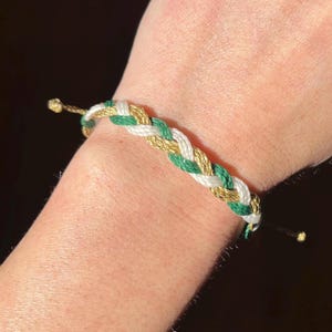 May include: A braided friendship bracelet with green, white, and gold threads.