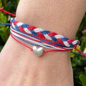 May include: A red, white, and blue braided friendship bracelet with a silver heart charm.