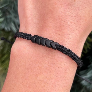 May include: A black braided bracelet with black arrow-shaped beads.