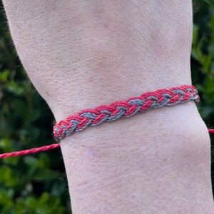 May include: A braided friendship bracelet with alternating red and gray strands.