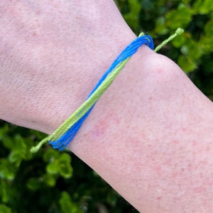 May include: A blue and green friendship bracelet on a person's wrist.