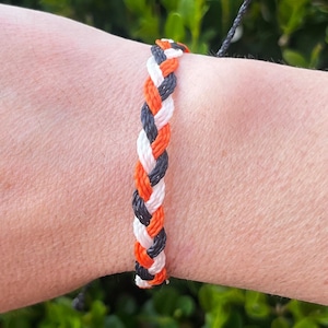 May include: A braided friendship bracelet with orange, white and black string.