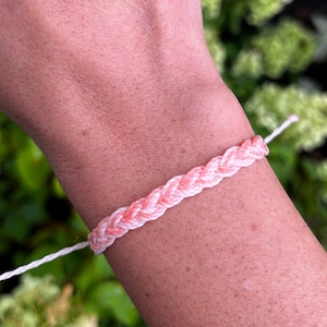 May include: A pink and white braided friendship bracelet on a person's wrist.
