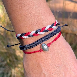 May include: Three braided friendship bracelets in red, white, and black with a silver football charm.