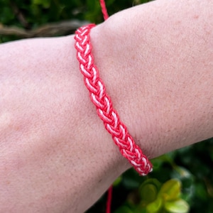 Peut inclure: Un bracelet d'amitié tressé rouge et blanc porté au poignet.