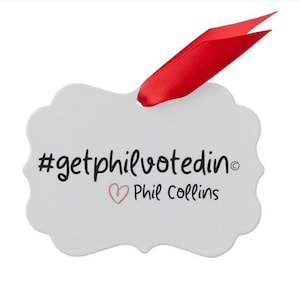 May include: White ceramic ornament with a red ribbon. The ornament has the text "#getphilvotedin" and "Phil Collins" with a heart symbol.