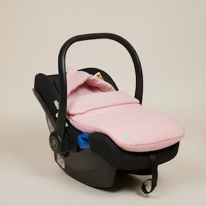 May include: A black infant car seat with a pink quilted cover and a black handle. The cover is a soft pink color and appears to be padded for comfort. The car seat has a blue release button.