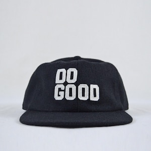 May include: A black baseball cap featuring the text DO GOOD embroidered in white block letters on the front. The cap has a structured crown and a flat brim, constructed from a felt-like material with a consistent dark texture throughout the surface.
