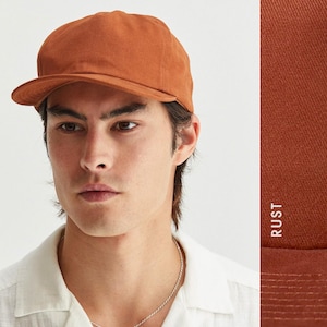 Puede incluir: Una gorra de b&eacute;isbol de color &oacute;xido con visera curva. La gorra est&aacute; hecha de una tela de color liso y tiene un dise&ntilde;o cl&aacute;sico y sin estructura. La palabra "RUST" est&aacute; impresa verticalmente en el lado derecho de la imagen.