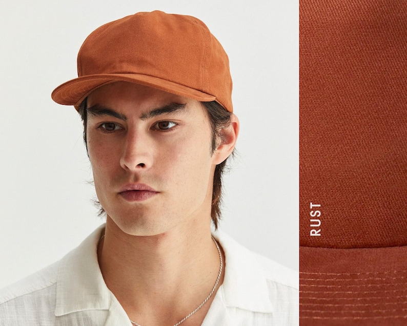 Puede incluir: Una gorra de b&eacute;isbol de color &oacute;xido con visera curva. La gorra est&aacute; hecha de una tela de color liso y tiene un dise&ntilde;o cl&aacute;sico y sin estructura. La palabra "RUST" est&aacute; impresa verticalmente en el lado derecho de la imagen.