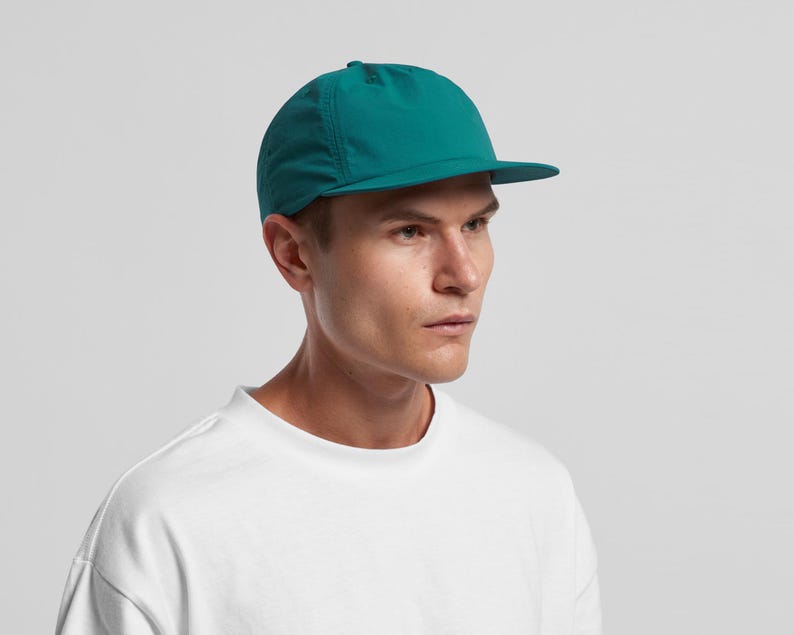May include: A teal baseball cap with a short peak. The cap is made of a lightweight material and has a simple design. The cap is worn by a person wearing a white t-shirt. The cap is a vibrant shade of teal.