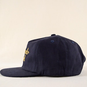 Puede incluir: Gorra de b&eacute;isbol azul marino con visera plana. La gorra presenta texto dorado bordado en la parte delantera. La gorra tiene un bot&oacute;n en la parte superior y una visera curva. Es un estilo cl&aacute;sico.