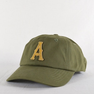 May include: Olive green baseball cap with a gold embroidered letter "A" on the front. The cap has a curved brim and an adjustable strap at the back. A casual accessory for everyday wear.