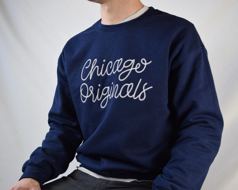 Puede incluir: Sudadera azul marino con la inscripci&oacute;n "Chicago Originals" en blanco en el pecho. La sudadera tiene cuello redondo y mangas largas. La persona lleva una camiseta interior blanca.