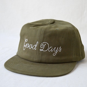May include: Olive green baseball cap with a curved brim. The phrase "Good Days" is embroidered in white cursive on the front. The cap has a button on top and a structured fit.
