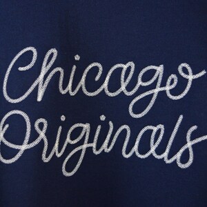 Puede incluir: Tela azul marino con las palabras "Chicago Originals" bordadas en blanco con escritura cursiva. El texto est&aacute; en una fuente decorativa y fluida, creando un dise&ntilde;o elegante.