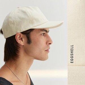 Puede incluir: Gorra de b&eacute;isbol color crema con visera curva. La gorra est&aacute; hecha de tela suave y tiene un dise&ntilde;o cl&aacute;sico y sencillo. El texto "EGGSHELL" est&aacute; impreso verticalmente en el lado derecho de la imagen.