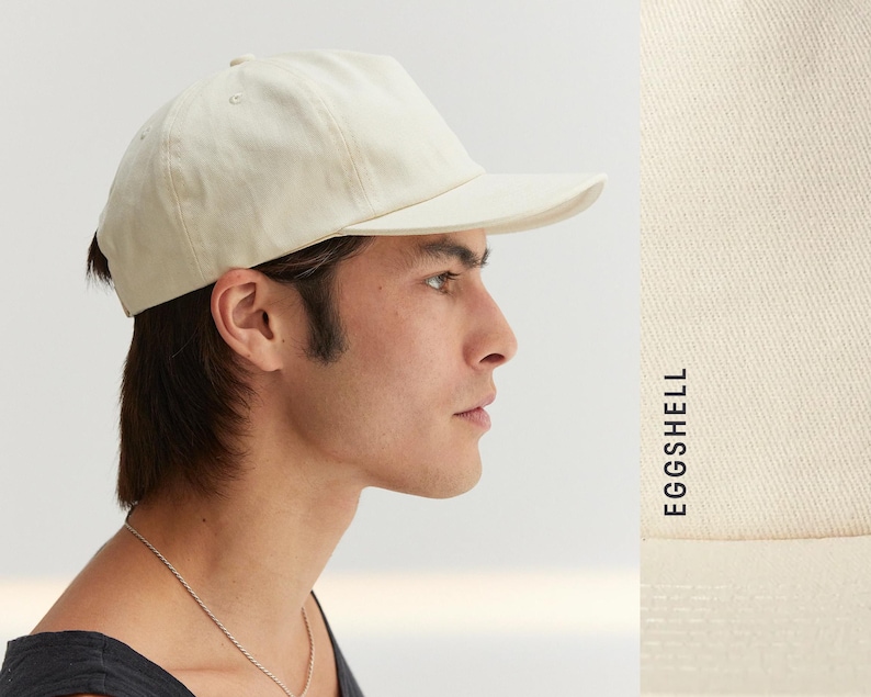 Puede incluir: Gorra de b&eacute;isbol color crema con visera curva. La gorra est&aacute; hecha de tela suave y tiene un dise&ntilde;o cl&aacute;sico y sencillo. El texto "EGGSHELL" est&aacute; impreso verticalmente en el lado derecho de la imagen.