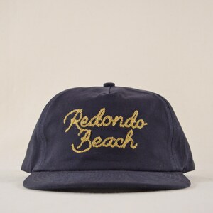 Puede incluir: Gorra de b&eacute;isbol azul marino con el texto bordado en oro "Redondo Beach". La gorra tiene una visera curva y una corona redondeada, adecuada para uso casual.