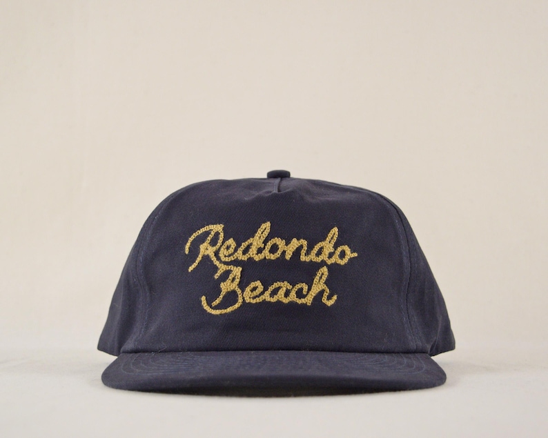 Puede incluir: Gorra de b&eacute;isbol azul marino con el texto bordado en oro "Redondo Beach". La gorra tiene una visera curva y una corona redondeada, adecuada para uso casual.