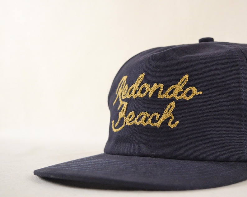 Puede incluir: Gorra de b&eacute;isbol azul marino con la inscripci&oacute;n bordada "Redondo Beach" en letras doradas. La gorra tiene una visera curva y una corona estructurada, ideal para protegerse del sol.