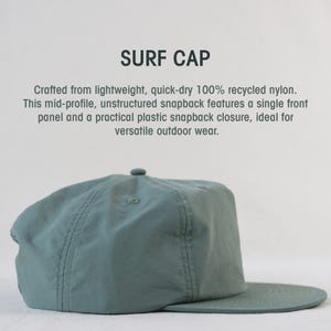 May include: A teal Surf Cap made from recycled nylon. The unstructured snapback hat has a single front panel and a plastic snapback closure. The text "SURF CAP" is at the top.