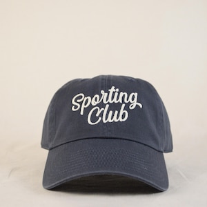 May include: A navy blue baseball cap with white embroidered text that reads "Sporting Club".
