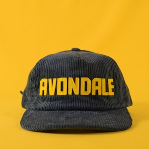 May include: A navy blue corduroy baseball cap with a yellow embroidered logo that reads "AVONDALE".