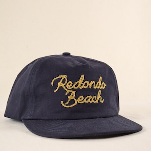 Puede incluir: Gorra de b&eacute;isbol azul marino con el texto bordado en oro "Redondo Beach". La gorra tiene una visera curva y una corona estructurada, adecuada para uso casual.