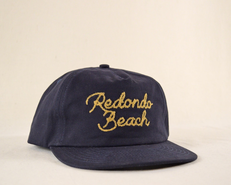 Puede incluir: Gorra de b&eacute;isbol azul marino con el texto bordado en oro "Redondo Beach". La gorra tiene una visera curva y una corona estructurada, adecuada para uso casual.