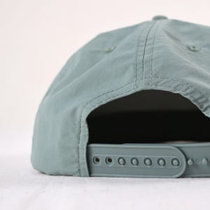 May include: A pale teal baseball cap with a curved peak and adjustable strap. The cap has a classic six-panel design with stitched seams and a plastic snap closure for a custom fit. The hat is made of a lightweight, durable material.